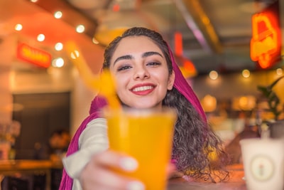 在白色长袖衬衫的女人举着橙色的塑料杯
